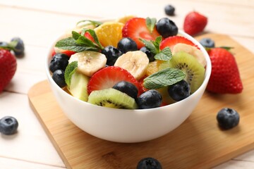 Tasty fruit salad in bowl and ingredients on wooden table, closeup