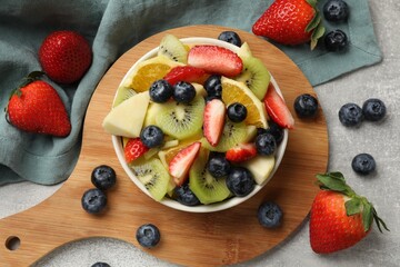Tasty fruit salad in bowl and ingredients on gray textured table, flat lay