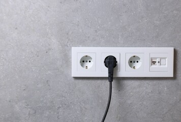 Power sockets and electric plug on grey wall, space for text