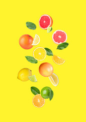 Many different fresh citrus fruits falling on yellow background