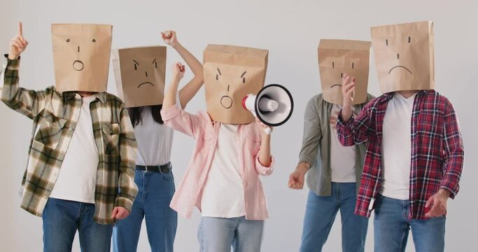 Faceless person in paper bag mask on head shouting in megaphone. Angry crowd of protesting people activists fighting for human rights on demonstration. Protest concept. 4k video. Slow motion video.