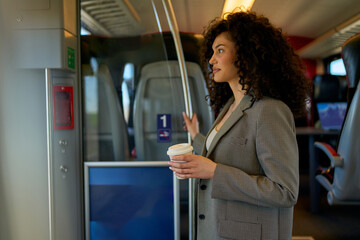 Fashionable female traveler with a coffee cup embracing the slow pace of city transport, gazing out...