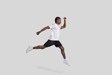 Athletic man in mid-air running pose on grey