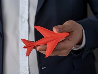 Businessman's hand holding a red paper airplane, representing corporate travel and innovation - 780398907
