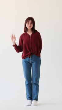 Optimistic Caucasian teenage girl greeting by waving hand on white background. Hello or goodbye concept, welcome concept. Vertical video.