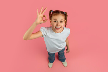 Happy girl showing OK sign on pastel pink