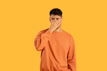 Man holding nose with displeased expression on yellow