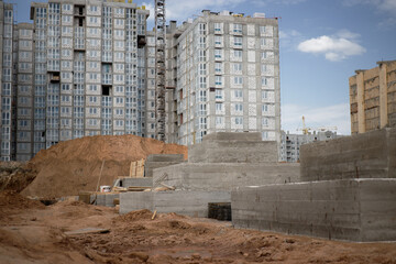 A pile of dirt rests beside a building under construction, where reinforced concrete foundations are being laid