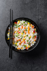 White rice with vegetables in a black bowl on black background. Top view