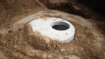 Installation of concrete sewer wells in the ground at the construction site. The use of reinforced concrete rings for cesspools, overflow septic tanks. Improvement of wells and storm sewage. - obrazy, fototapety, plakaty
