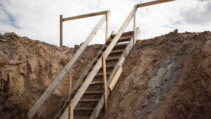Descent into a deep pit during the construction of the building. Safety in construction. Ladder for descending to reinforced concrete foundations. Ladder to success. Wooden ladder for workers. © Anoo