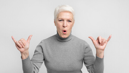 Surprised senior woman gesturing jumbo sign on grey background