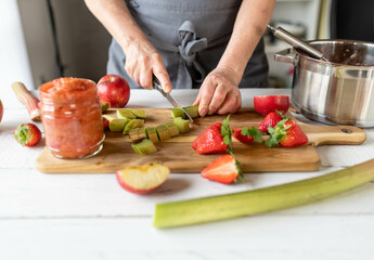 Woman cutting fresh rhubarb on a cutting board for making compote