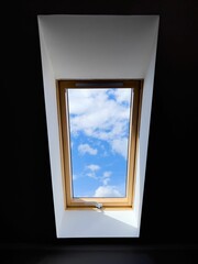 Vertical of the bright, cloudy sky seen from a ceiling window in a dark room