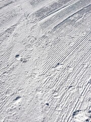 Vertical closeup of sunlit snow flows with footsteps on
