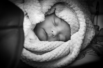 Black and white image of a peaceful newborn baby sleeping, swaddled in a soft, textured blanket, conveying a sense of calm and innocence.