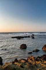 Fotobehang Vertical shot of a beautiful sea captured from a rocky shore during a scenic sunset © Wirestock