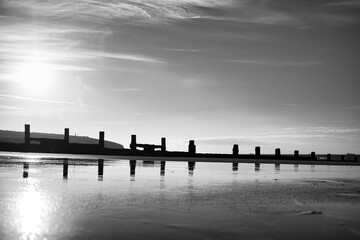 Grayscale shot of the breakwater with reflection in the sea in Sandow bay, Isle of Wight