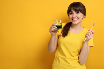 Young woman with mouthwash and toothbrush on yellow background, space for text