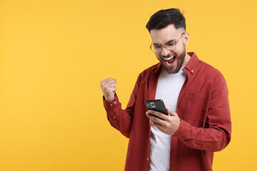 Happy young man using smartphone on yellow background, space for text