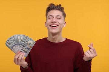 Happy man with dollar banknotes showing money gesture on yellow background