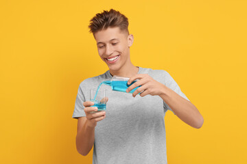 Young man using mouthwash on yellow background