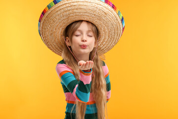 Cute girl in Mexican sombrero hat blowing kiss on orange background