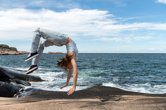 Full length side view of young woman doing somersault on rock by sea