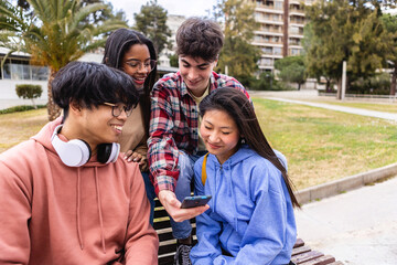 Happy student friends using mobile phone together sitting at college campus. Education and...