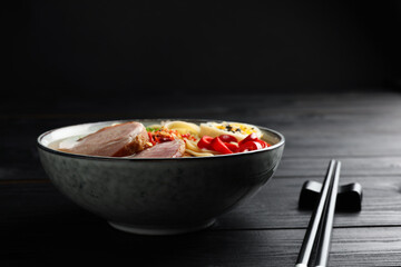 Delicious ramen in bowl and chopsticks on black wooden table, closeup. Noodle soup