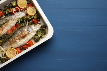 Delicious fish with vegetables and lemon in baking dish on blue wooden table, top view. Space for text