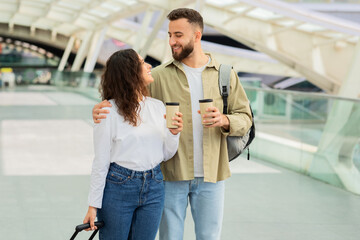 Happy Couple Walking Through an Airport With Takeaway Coffee