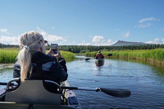 Senior woman photographing man kayaking in river on sunny day