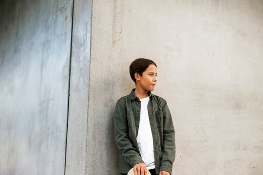 Pre-adolescent boy with unbuttoned green shirt leaning on wall