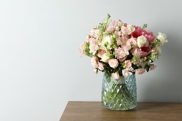Beautiful bouquet of fresh flowers in vase on wooden table near light wall, space for text