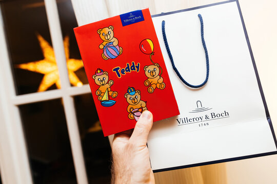 Paris, France - Mar 9, 2024: A male hand holds a teddy red package with bears drawn, revealing German-made cutlery set Villeroy and Boch in a red package. Starry background adds enchantment