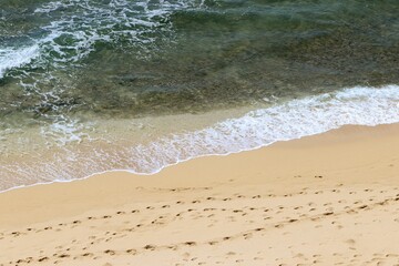 Beautiful shot of waves on a sunny beach with footprints on the sand at Diamond Head beach in Hawaii