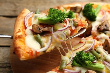 Taking piece of delicious vegetarian pizza at wooden table, closeup