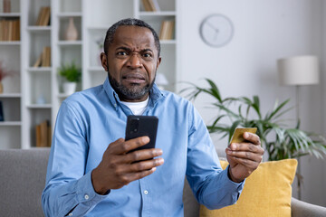 Focused man sitting at home with credit card and smartphone, possibly a victim or perpetrator of...