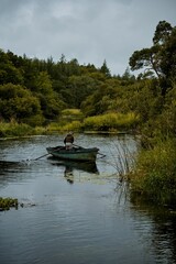 Vertical shot of a man in the small boat in a lake surrounded by a forest on a gloomy day