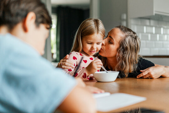 Woman kissing cute girl eating breakfast at dining table