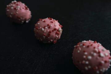 Closeup of delicious pink cake balls with colorful frosting isolated on a dark background