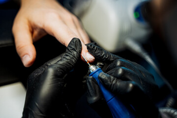 A person in black gloves polishes their nails with an electric blue machine