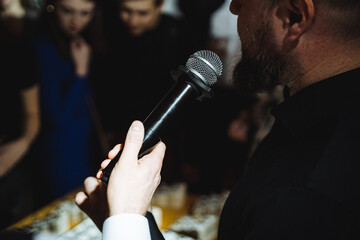A man gestures with a microphone, performing for a crowd at a music event