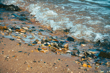 Closeup of small stones on a sandy beach with waves