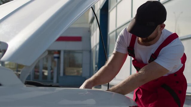 Amidst open hood of vehicle skilled mechanic tends to repairs displaying his mastery in art of car maintenance. Mechanic watches closely to detail involved in automotive repair at auto service.