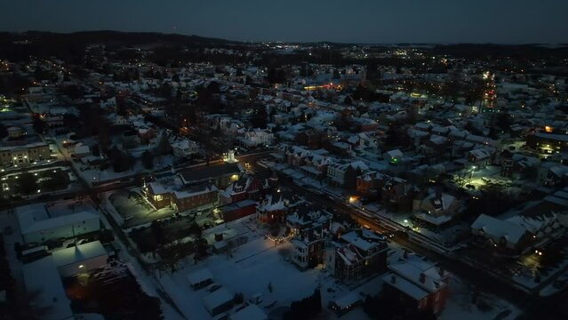 Warm Lighting Snowy City in America at winter snow night. Driving cars on road. Aerial orbit shot of illuminated cityscape.