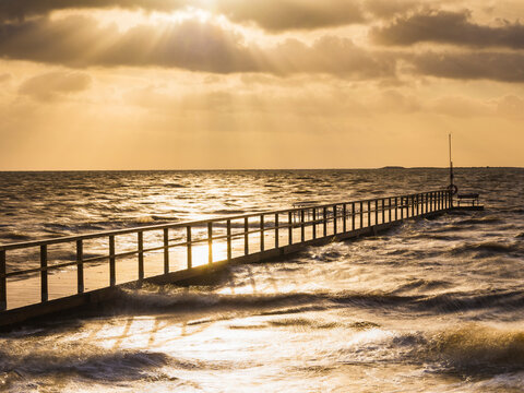 Wooden jetty with railing in sea during sunset