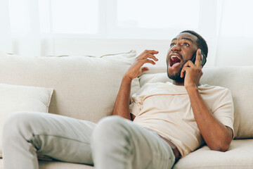 Happy African American Man Sitting on a Black Sofa, Talking on his Mobile Phone and Having a Video...