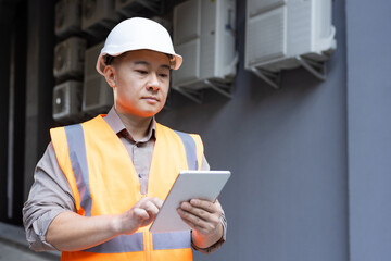 Young Asian male engineer, construction worker standing outside building and using tablet